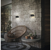 Moderne rechteckige LED Wandleuchten montiert an einer Natursteinmauer über einem Sitzbereich mit Rattan Sessel und Beistelltisch.