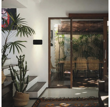 Moderne Wandleuchte in einem hellen Wohnraum mit Treppe und Blick auf eine Terrasse mit Rattanmöbeln.