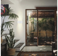 Moderne Wandleuchte in einem lichtdurchfluteten Wohnbereich mit Treppe, Pflanzen und Blick auf eine Terrasse durch eine große Glasschiebetür.