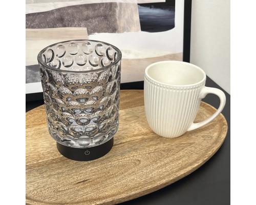 LED Tischleuchte aus Glas mit strukturierter Oberfläche auf einem Holztablett neben einer Tasse.