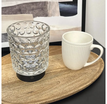 Eine strukturierte Glaslampe mit schwarzem Sockel und Ein Aus Schalter neben einer gerippten Tasse auf einem ovalen Holztablett.