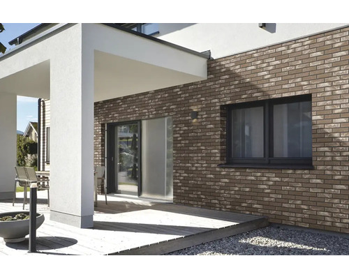Moderne Hausfassade mit Klinkerriemchen an einer Terrasse mit Holzbelag und einem weißen Vordach.