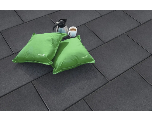 Dunkle Terrassenplatten in Rechteckform mit zwei grünen Sitzkissen, einer Kaffeekanne und einer Kaffeetasse auf einer ebenen Bodenfläche.