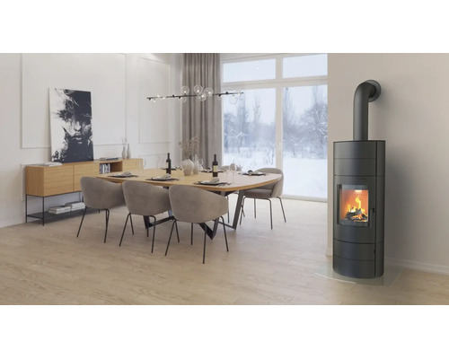 Moderner Kaminofen in einem hellen Esszimmer mit Holztisch und Stühlen vor einer Fensterfront mit Blick auf eine verschneite Winterlandschaft.