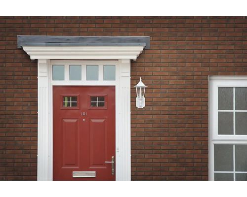 Eingangsbereich eines Hauses mit roter Haustür, weißem Türrahmen und Wandlampe an einer Ziegelfassade.