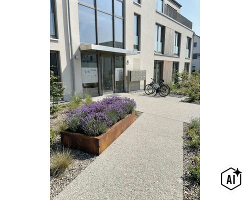 Moderne Wohnanlage mit rechteckigem Pflanzkübel aus Cortenstahl bepflanzt mit Lavendel vor dem Hauseingangsbereich und Fahrradständer. (Image AI modified or generated)
