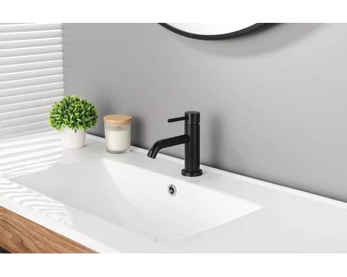 Moderne schwarze Waschtischarmatur an einem weißen Waschbecken in einem Badezimmer mit Zimmerpflanze und Kerze.