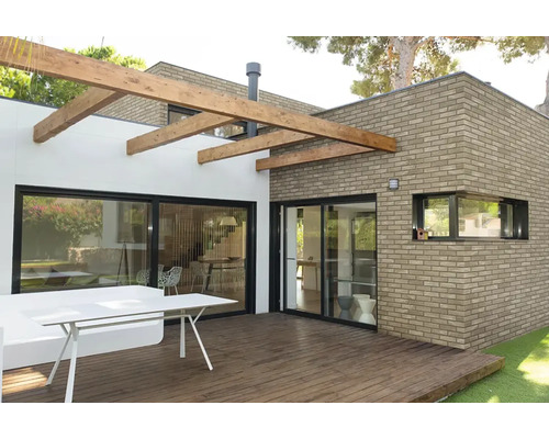 Moderne Terrasse mit Holzdeck und Pergola vor einem Wohnhaus aus Mauerwerk und weißen Wänden mit großen Schiebetüren.