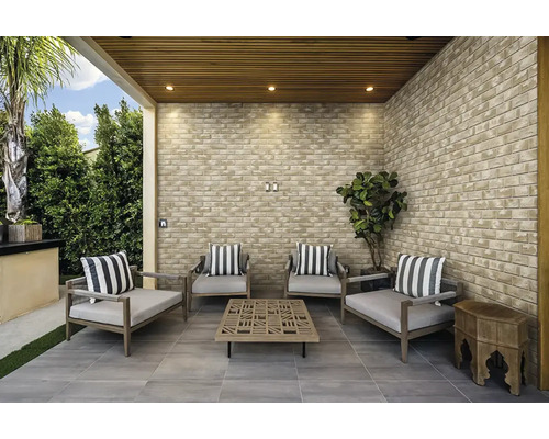 Moderne überdachte Terrasse mit Verblendern in Ziegeloptik, Sitzgruppe aus Holzsesseln mit Kissen und quadratischem Couchtisch auf Fliesenboden.
