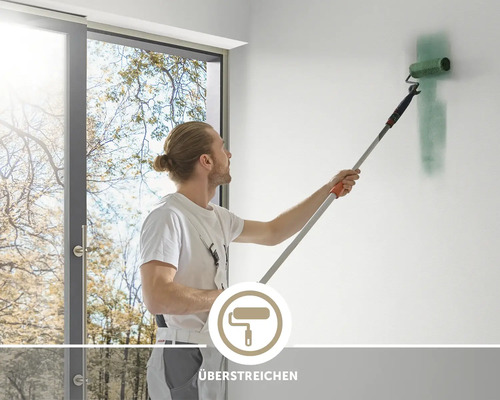 Handwerker streicht mit einer Farbrolle an einer Teleskopstange eine Zimmerwand, Symbol für das Überstreichen von Wandflächen.