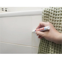 Person verwendet Edding 8200 Fugenmarker zum Auffrischen von Fliesenfugen an einer Wand in einem Badezimmer.