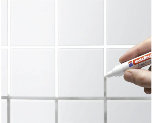 Hand hält einen Edding Fugenmarker zur Ausbesserung von Fliesenfugen an einer gekachelten Wand.
