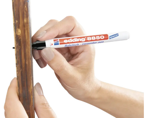 Eine Hand nutzt einen Edding 8850 Bohrlochmarker zum Markieren an einer Holzleiste.