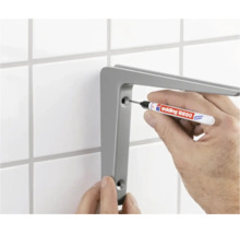 Eine Person markiert mit einem Edding 8850 Spezialmarker die Bohrlöcher für einen Wandregalträger an einer gefliesten Wand.