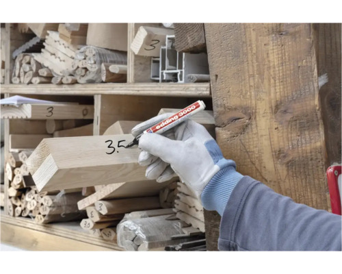 Person mit Arbeitshandschuh beschriftet Holzbalken mit einem Edding 3000 Permanentmarker in einem Holzlager.
