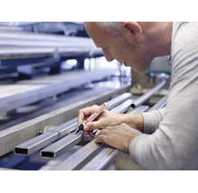Handwerker markiert mit einem Edding 3000 Permanentmarker ein Metallprofil an einer Werkbank.