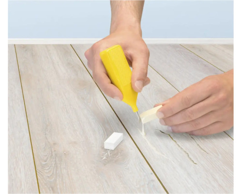 Eine Person repariert einen Laminatboden mit einem Reparaturwachs und einem Schmelzer.