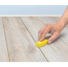 Eine Hand verwendet einen Reparaturwachsstift zur Ausbesserung von Kratzern auf einem Holzlaminatboden.