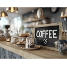 Eine Kuchentheke in einem Cafe mit einer Tafel auf der Coffee steht und einer kleinen Glasglocke mit einem Gebäck auf dem Tresen.