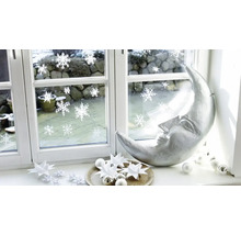 Weihnachtsdekoration auf einer Fensterbank mit silberner Mondsichel, Papiersternen und Fensterstickern mit Schneeflockenmotiv.