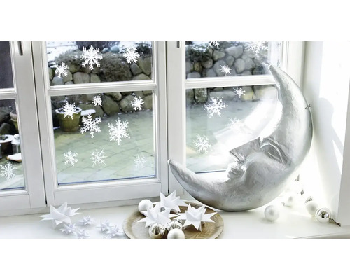 Weihnachtsdekoration auf einer Fensterbank mit silberner Mondsichel, Papiersternen und Fensterstickern mit Schneeflockenmotiv.