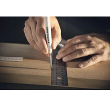 Eine Hand nutzt einen Edding 8880 Tieflochmarker und ein Lineal, um eine Markierung auf einem Holzbrett vorzunehmen.