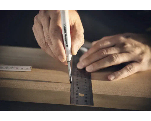 Eine Hand nutzt einen Edding 8880 Tieflochmarker und ein Lineal, um eine Markierung auf einem Holzbrett vorzunehmen.