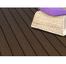 Dunkle Terrassendielen aus Holz mit einem geflochtenen Korbsessel und einem lila Kissen auf einer Terrasse.