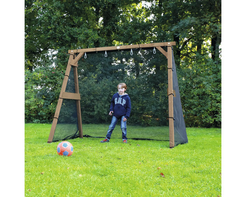 Ein Junge spielt Fußball vor einem hölzernen Fußballtor mit integriertem Fangnetz auf einer Wiese im Garten.