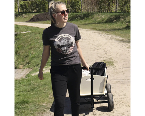 Eine junge Frau zieht einen Bollerwagen aus Holz mit Gummirädern auf einem Feldweg im Freien.