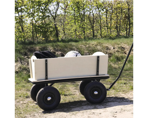Ein Bollerwagen aus Holz mit vier großen Luftreifen steht auf einem Waldweg und ist mit einem Ball und einer Tasche beladen.