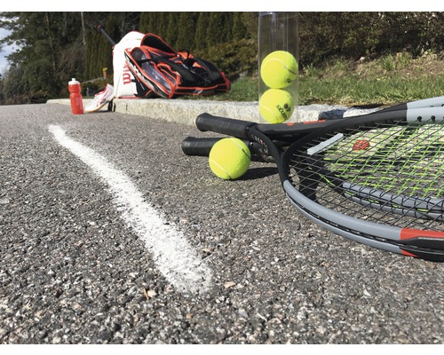 Tennisschläger, Tennisbälle, Tennistasche und Trinkflasche auf Asphalt