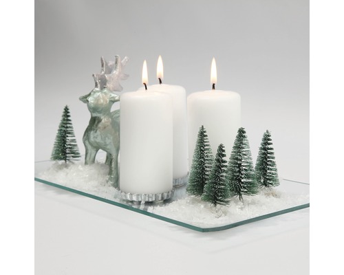 Weihnachtsdekoration mit Kerzen, Rentierfigur und Tannenbäumen auf einer Glasplatte