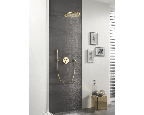 Duschszene mit Kopfbrause, Handbrause und Brausearmatur in Goldoptik vor dunkler Wand.