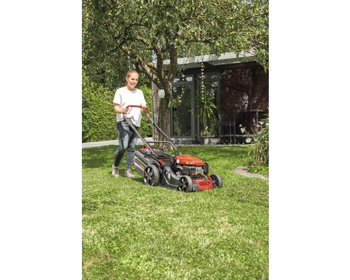 Frau benutzt einen Rasenmäher im Garten.