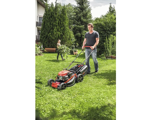 Mann mäht Rasen mit einem Rasenmäher im Garten.