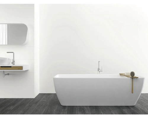 Badezimmer mit Badewanne, Waschbecken und Spiegel an weiß gefliesten Wänden und dunklem Holzboden