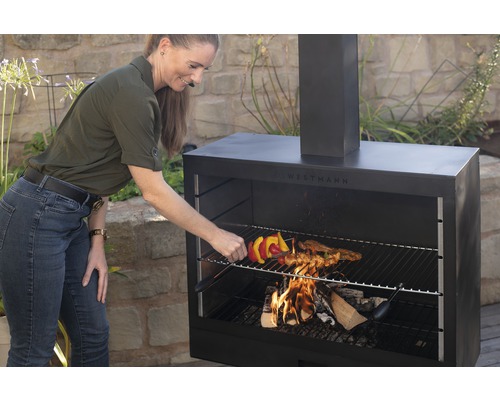 Frau grillt Fleischspieß auf einem Westmann Grillkamin im Freien