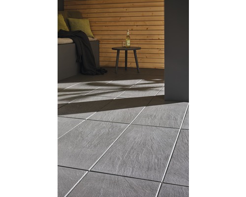 Terrasse mit grauen Fliesen, Holzwand und kleinem Tisch.