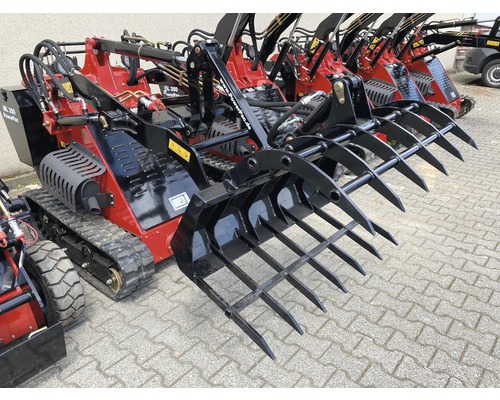 Mehrere rote PowerPac Minilader mit schwarzen Anbaugeräten stehen auf einem gepflasterten Untergrund.
