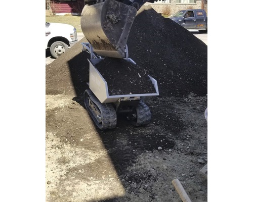 Mini-Dumper mit Raupen und Erde wird von Bagger befüllt