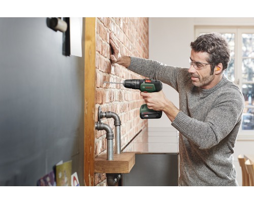 Mann bohrt mit einem Akku-Bohrschrauber in eine Ziegelwand