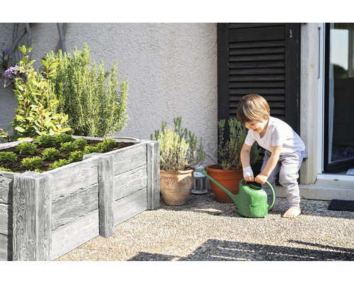 Junge gießt Pflanzen in einem Hochbeet und Pflanzkübeln im Garten.