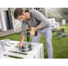 Mann bohrt mit einem Akku-Bohrschrauber Löcher in einen Metalleimer im Garten.
