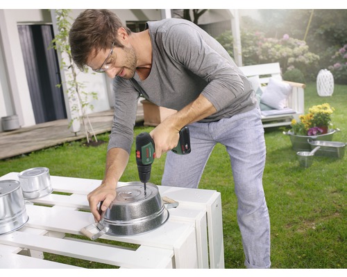 Mann bohrt mit einem Akku-Bohrschrauber Löcher in einen Metalleimer im Garten.