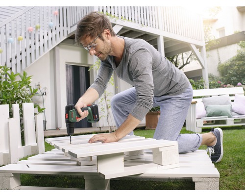 Mann arbeitet mit einem Akkuschrauber an einem DIY-Projekt aus Paletten im Garten.