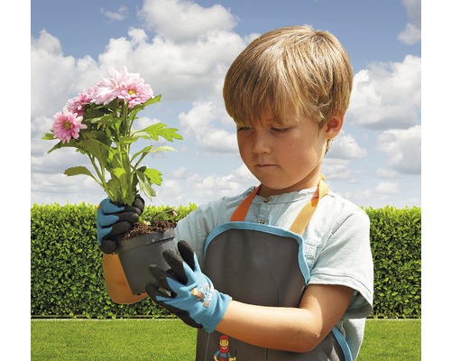 Junge mit Gartenschürze und Gartenhandschuhen hält eine Topfpflanze mit rosa Blüten.