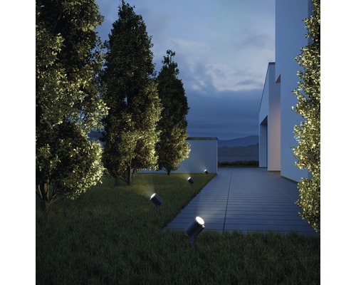 Außenansicht eines modernen Hauses mit Rasen und Bäumen, die von mehreren Strahlern beleuchtet werden.
