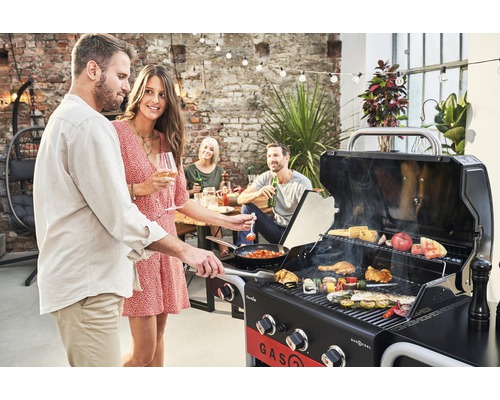 Personen grillen mit einem Gasgrill im Freien, wobei verschiedene Lebensmittel auf dem Grill zubereitet werden.
