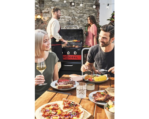 Eine Gruppe von Personen genießt ein Barbecue im Freien mit einem Holzkohlegrill und einer Vielzahl von Speisen.